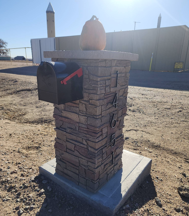 A stone mailbox pillar on a concrete pad labeled 