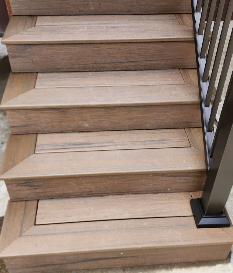 Close-up of brown composite wood steps with a mitered border and a black metal railing on the right side.
