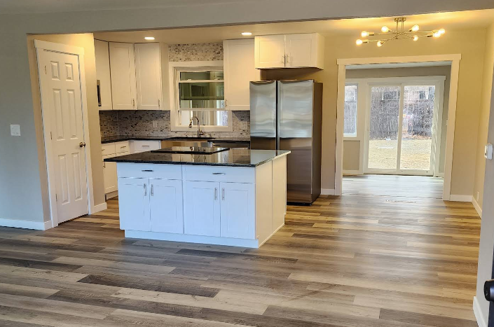 A modern, open-concept kitchen featuring white cabinetry, a black island countertop, stainless appliances, and wood floors.