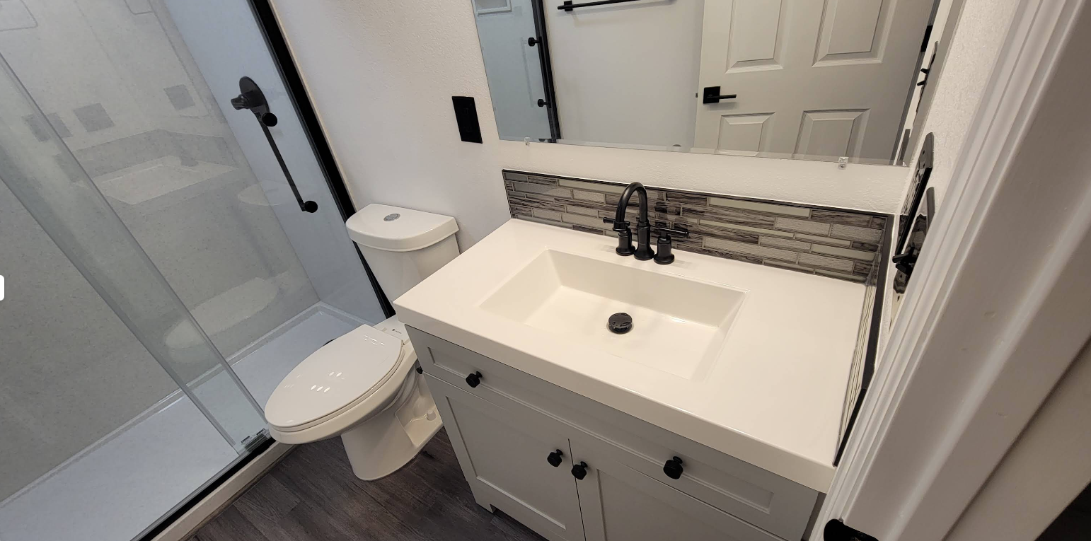Modern bathroom with a white vanity, a grey-tiled backsplash, a rectangular sink, a toilet, and a glass-enclosed shower.