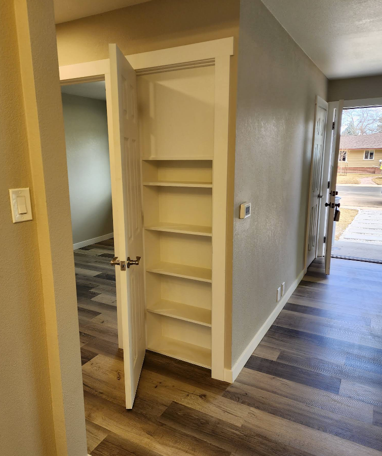 Interior hallway with wood-look flooring, a pantry with five open shelves, and a doorway leading to the outdoors.