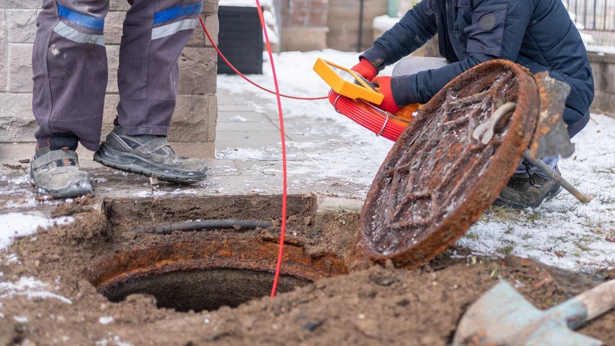 Workers with tools open a manhole in snowy ground.