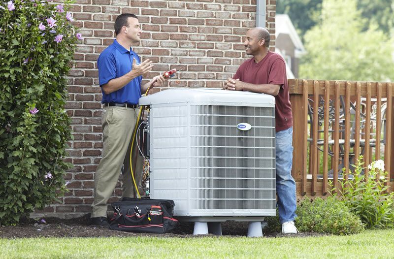 An HVAC technician discusses air conditioner maintenance with a homeonwer.