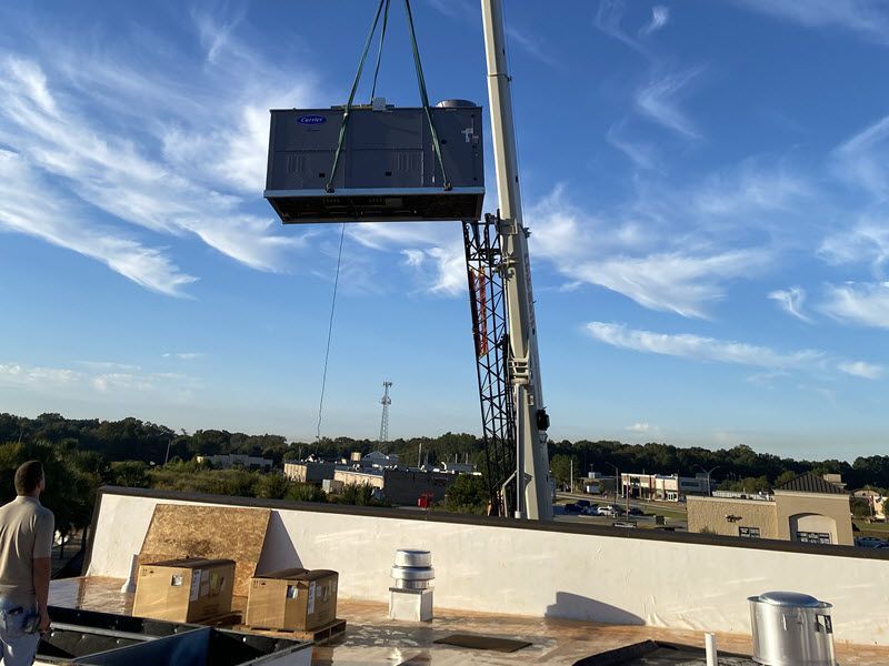 A crane lifts an HVAC unit onto a building roof.
