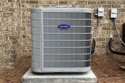 A Carrier heat pump in front of a brick building exterior.