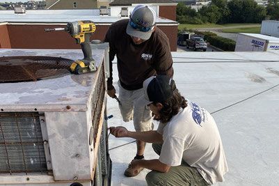 Two men service an old HVAC unit.