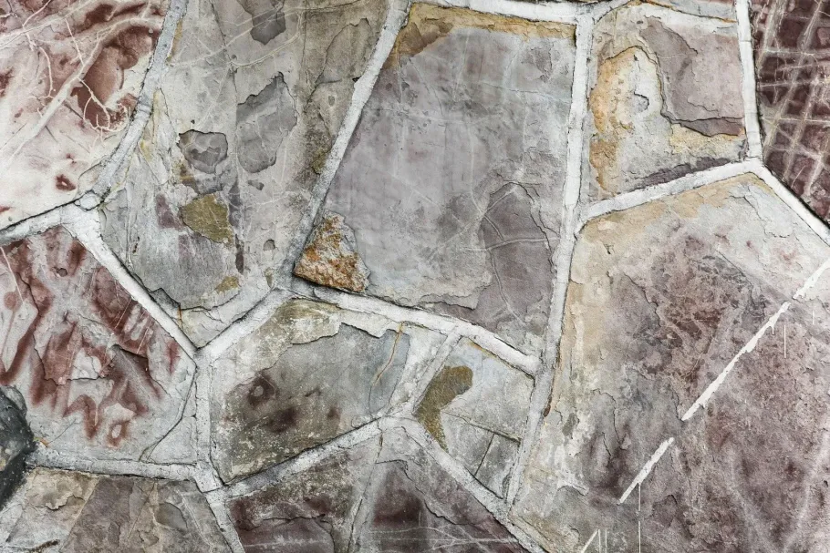 A close-up of a rustic, uneven flagstone patio with light gray grout lines between irregular, multicolored stone slabs.