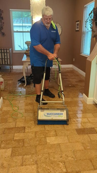 A man is cleaning a tile floor with a machine in a living room.