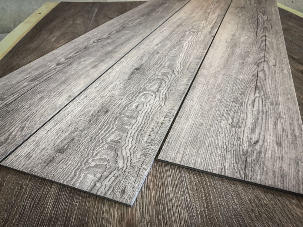 Three grey-toned wood-look planks arranged on top of darker wood, showing wood grain detail. — TNT Floor Removal & Demolition in Tewantin, QLD