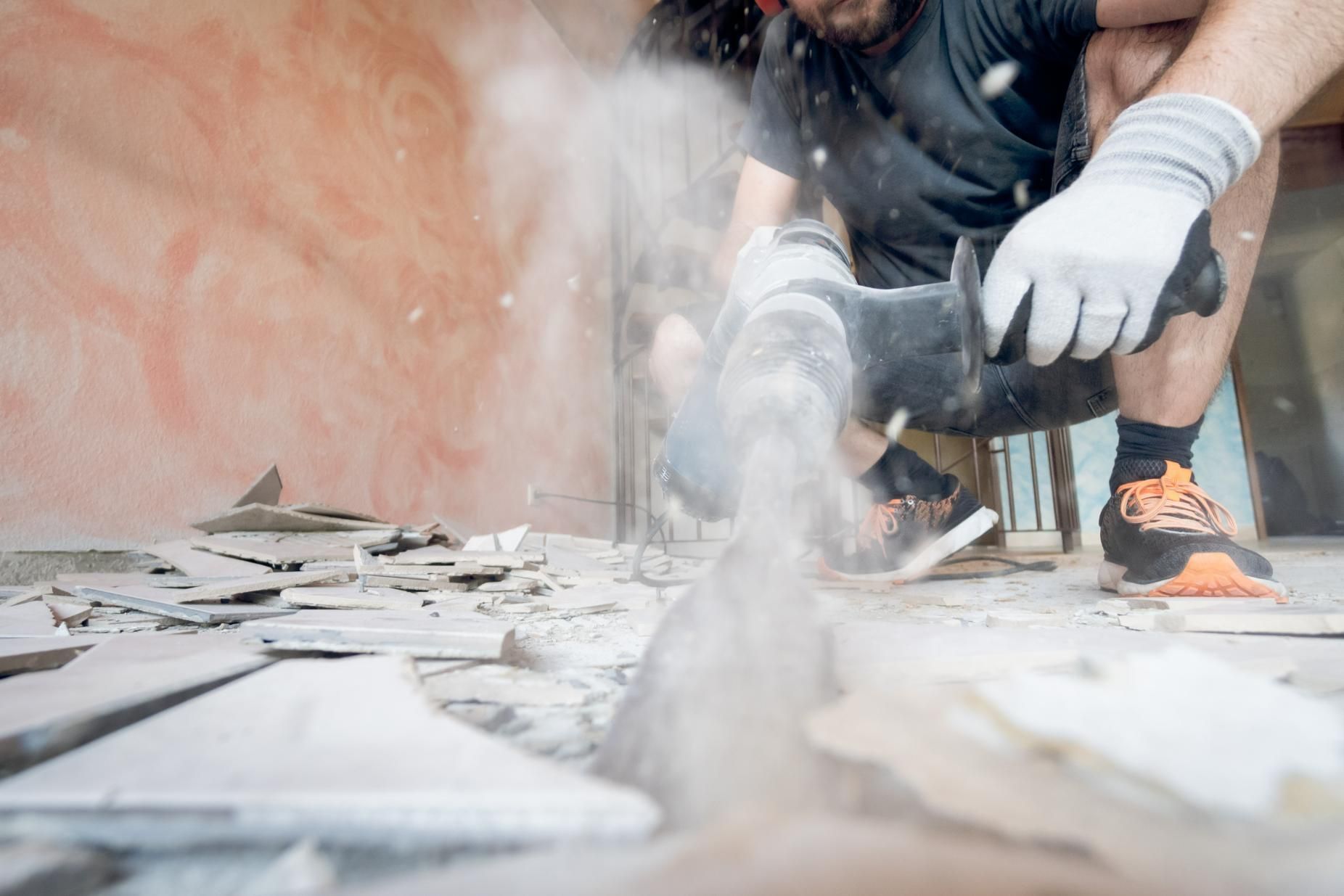 A Man Is Using a Drill to Break Tiles on The Floor — TNT Floor Removal & Demolition in Tewantin, QLD
