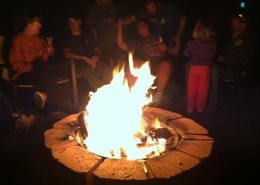 A group of people are sitting around a fire pit at night