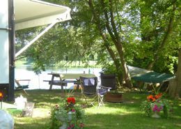 A rv parked in a grassy area next to a lake with a picnic table and chairs.