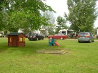 A small house is sitting in the middle of a grassy field next to a sandbox.