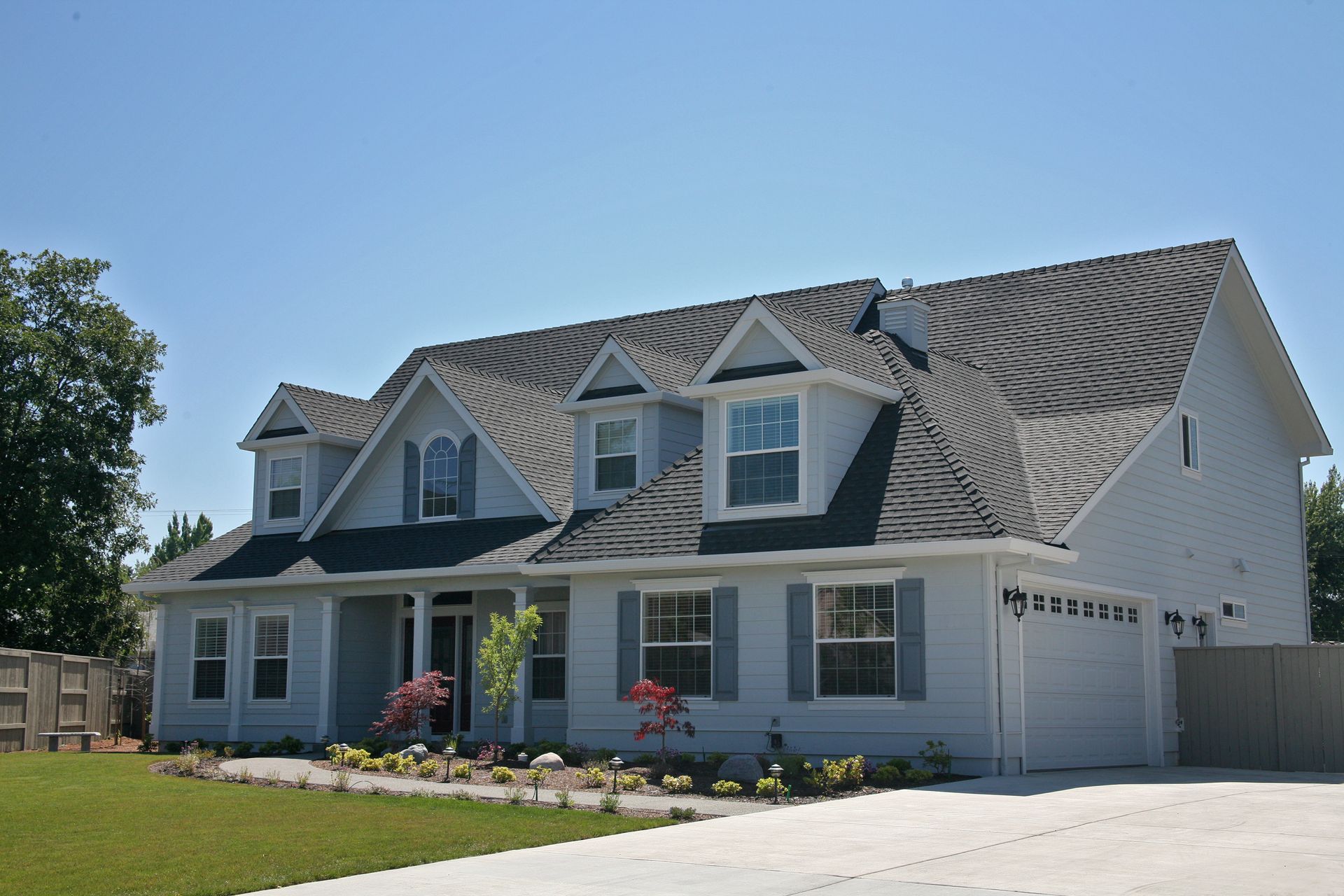 Light blue two-story house with gray roof and garage, blue shutters, and a green lawn under a clear blue sky.