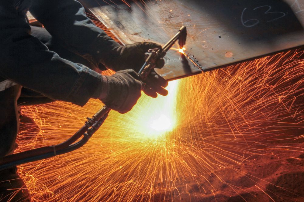 A man is cutting a piece of metal with a torch.