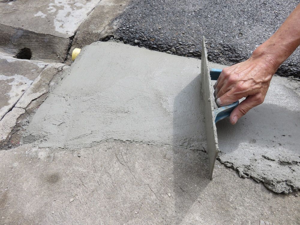 A person is using a trowel to spread concrete on the ground.