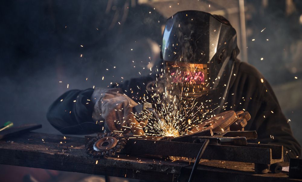 A man wearing a welding mask is welding a piece of metal.