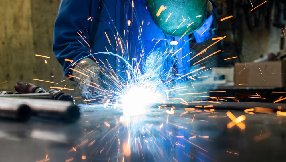 A man is welding a piece of metal in a factory.