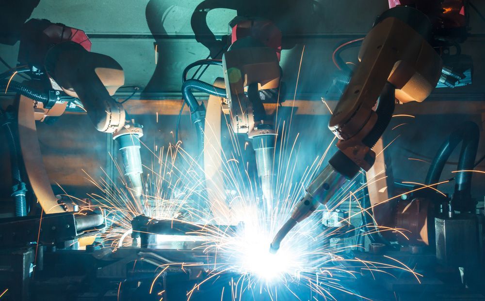 A group of robots are welding a piece of metal in a factory.