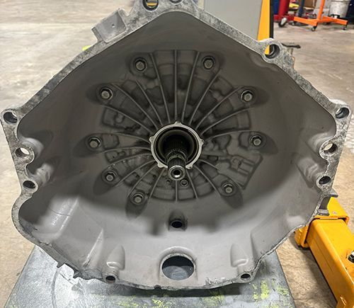 The bell housing of a mechanical transmission, showing the interior cavity, input shaft, and mounting bolt holes.