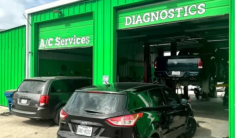A bright green auto repair shop with an A/C services bay and a diagnostics bay, featuring a truck on a lift and two cars.