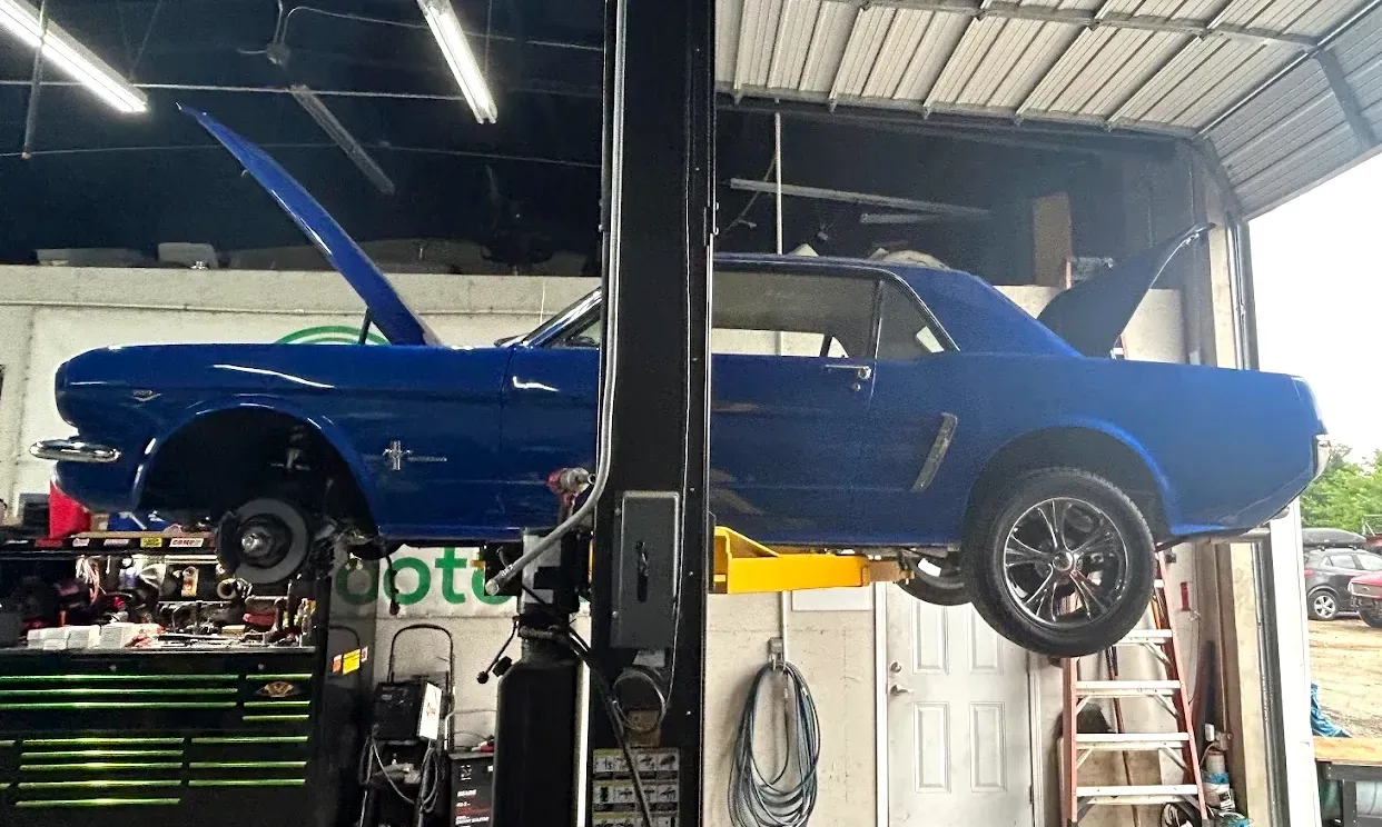 A classic blue Ford Mustang raised on a hydraulic lift inside an automotive repair shop with its hood and trunk open.