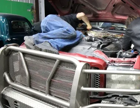 A person kneels across the engine bay of a red truck while working on the engine in a repair shop.