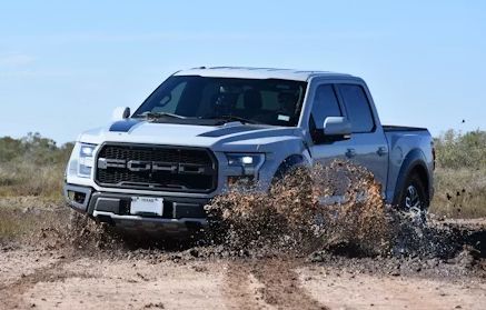 Gray pickup truck driving through a dusty off-road desert trail under a blue sky