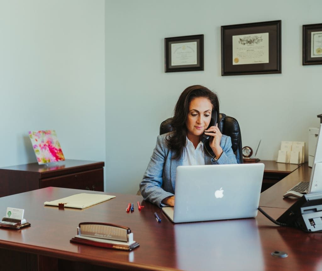 A woman is sitting at a desk with a laptop and talking on a cell phone.