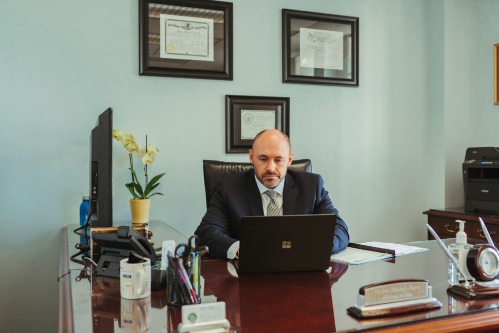 A man in a suit and tie is sitting at a desk using a laptop computer.