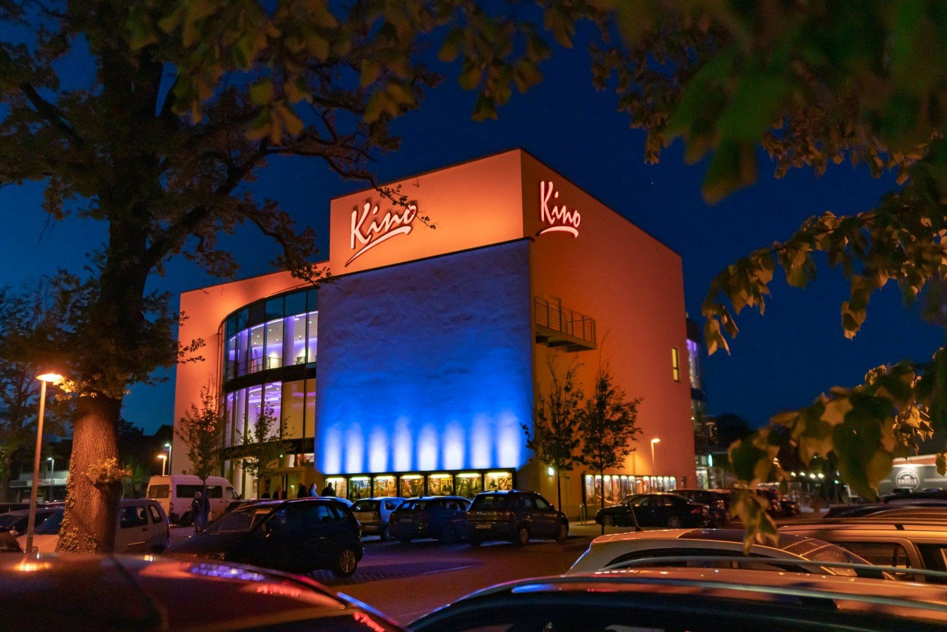 Ein großes Gebäude, vor dem nachts viele Autos parken.