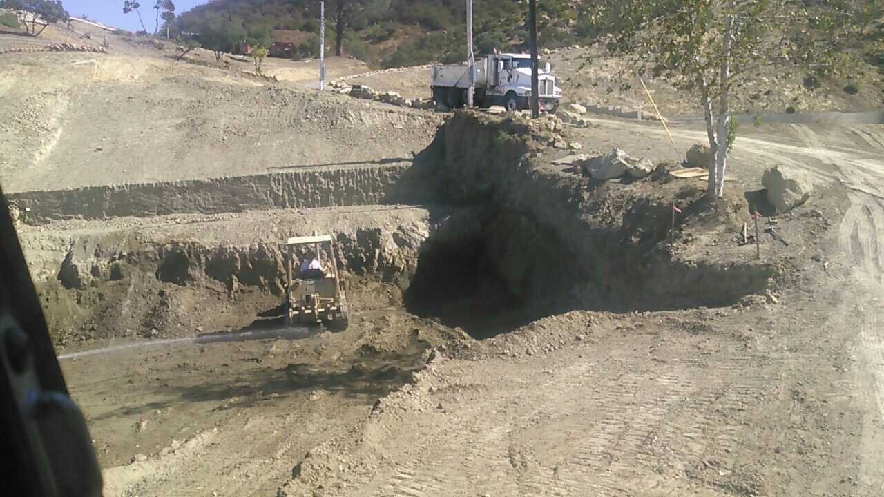 A truck is driving down a dirt road next to a bulldozer