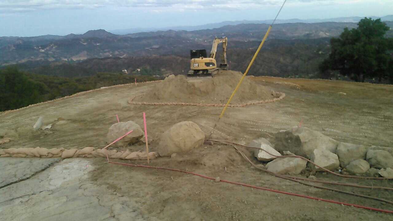 A yellow excavator is sitting on top of a dirt hill.