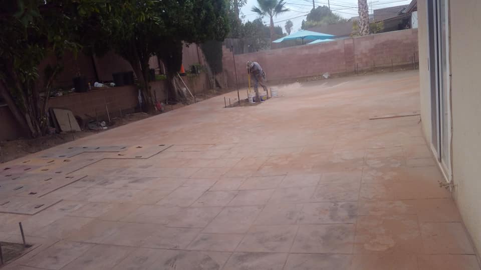 A man is working on a patio in a backyard.
