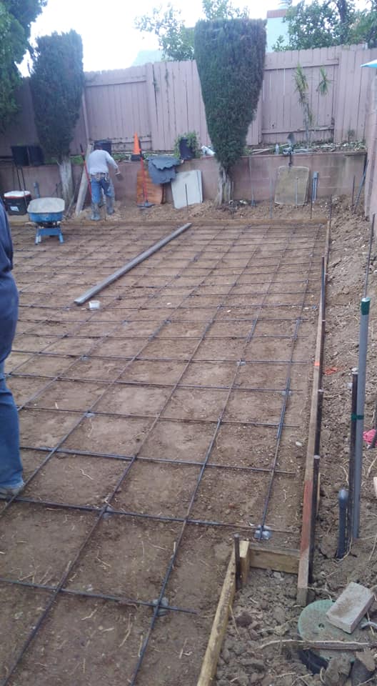 A person is standing on a concrete slab in a backyard.