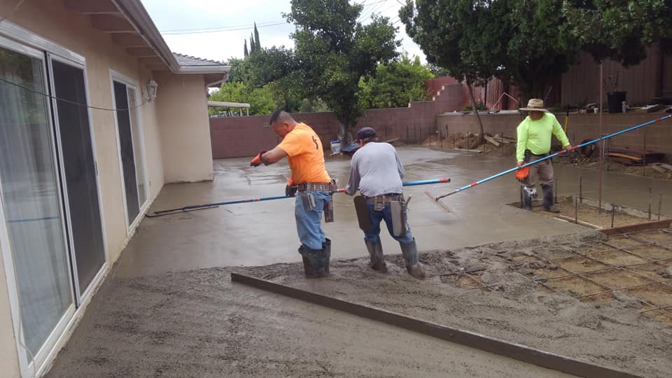 Three men are working on a concrete driveway in front of a house.