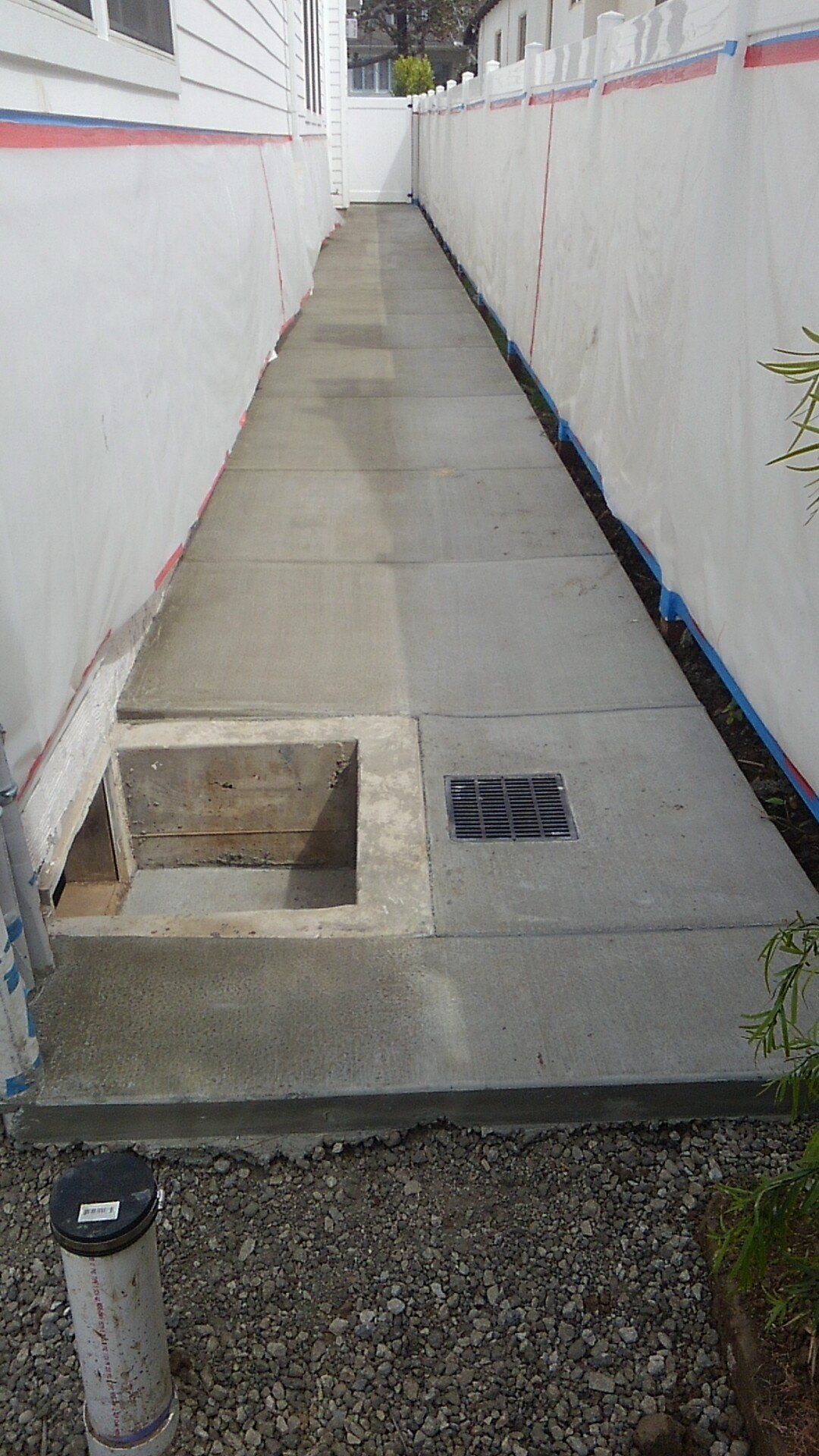 A concrete walkway between two buildings with a drain on the side of it.