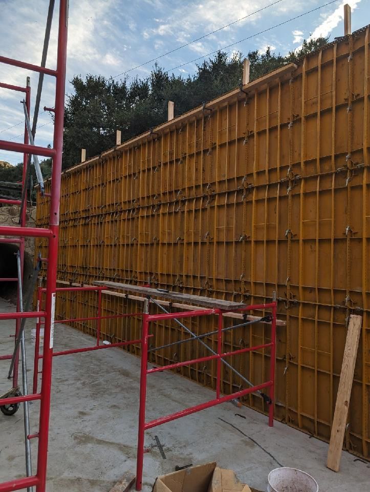 A large wall is being built with scaffolding and a red railing.