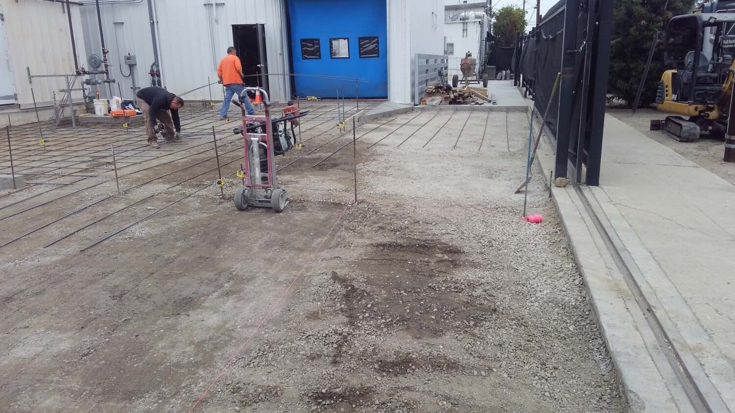 A group of construction workers are working on a concrete driveway in front of a building.