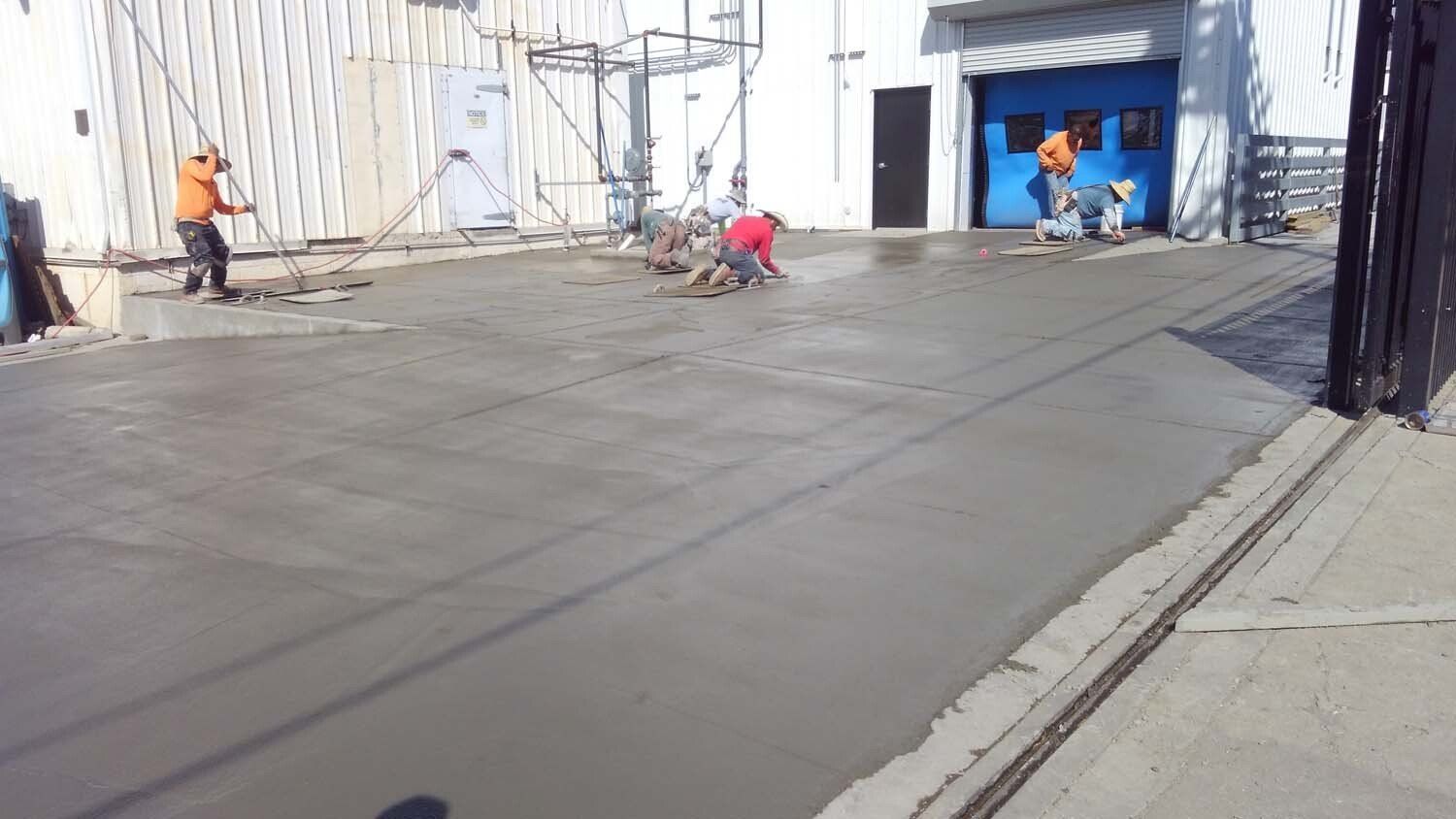 A group of construction workers are working on a concrete driveway
