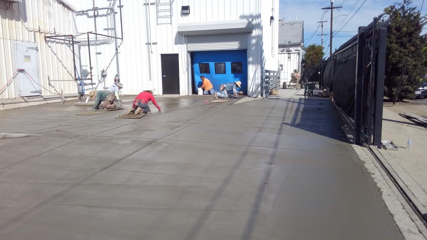 A group of people are working on a concrete driveway in front of a building.