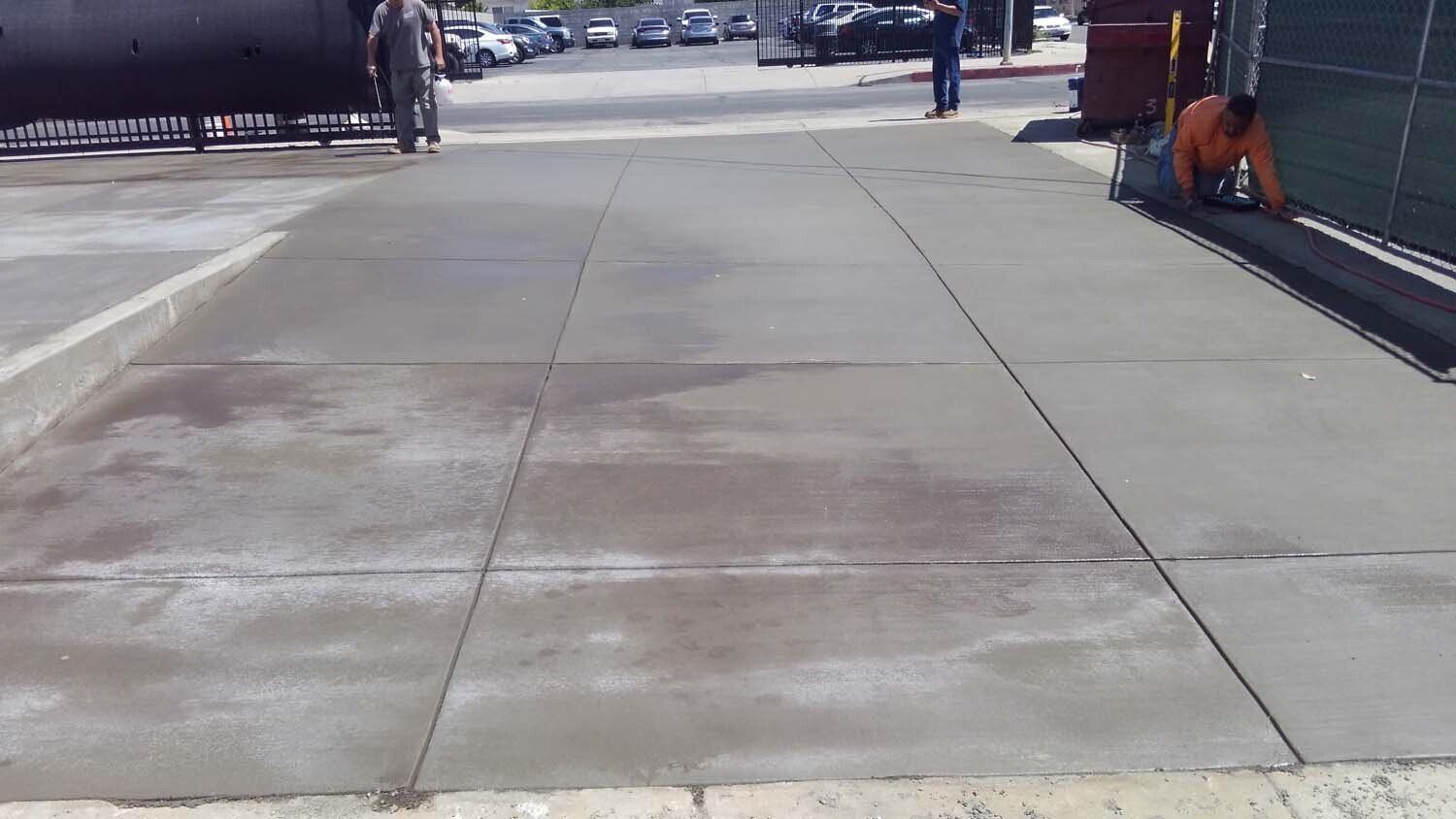 A man is working on a concrete sidewalk in a parking lot