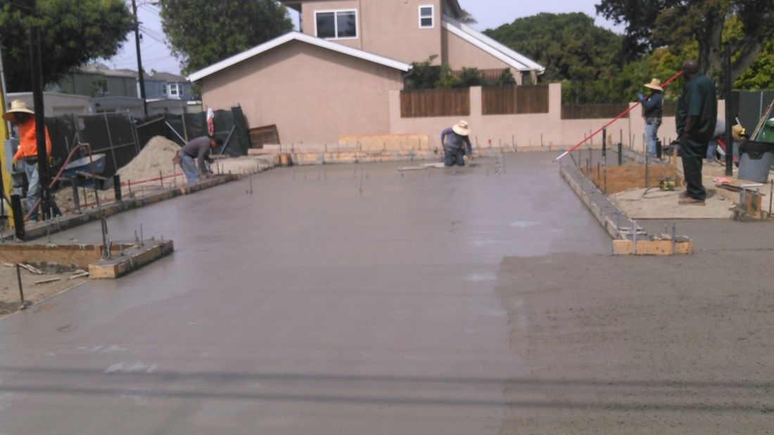 A group of construction workers are working on a concrete driveway in front of a house.