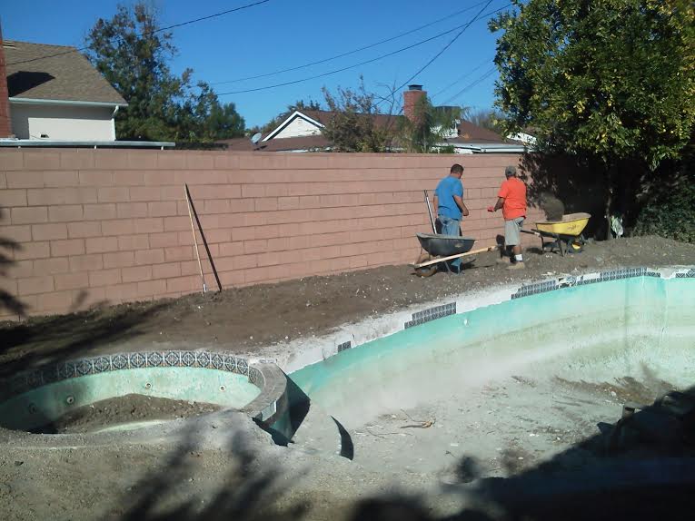 A man is pushing a wheelbarrow next to a swimming pool