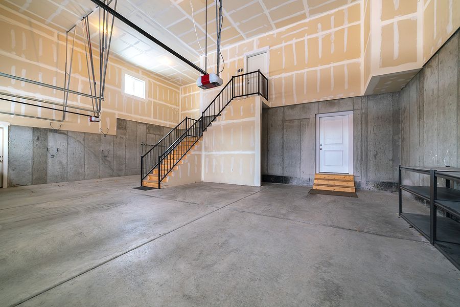 Empty garage with concrete floor, unfinished walls, stairs to an upper level, and a door.