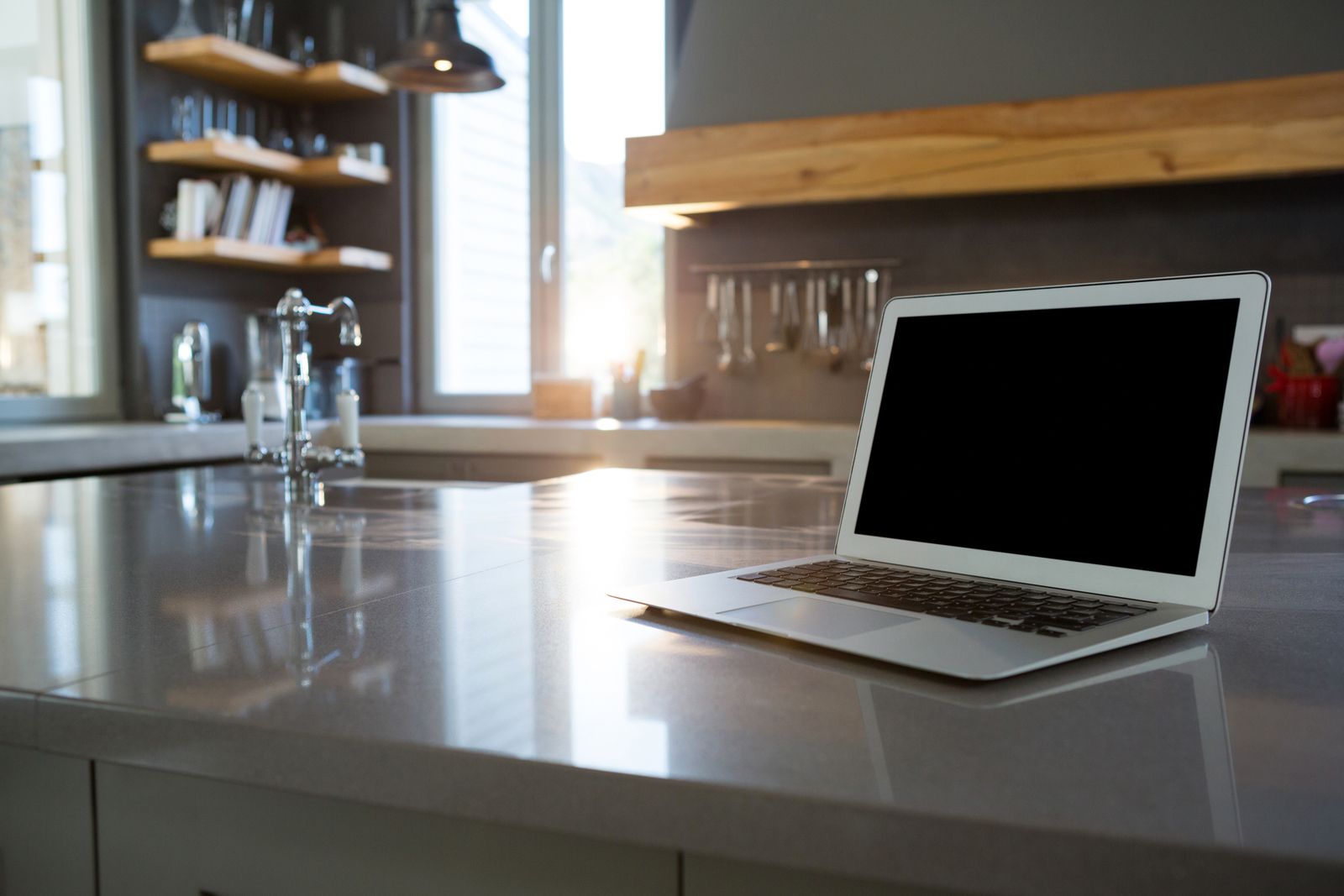 Laptop on a kitchen counter with a window in the background.