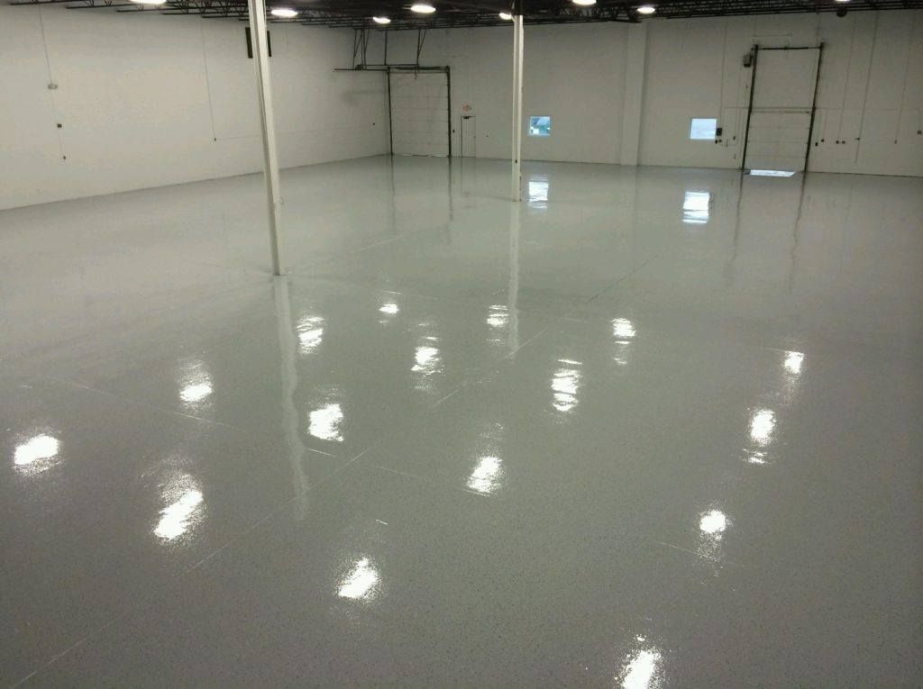 A large, empty room with a shiny, light gray epoxy floor and white walls.