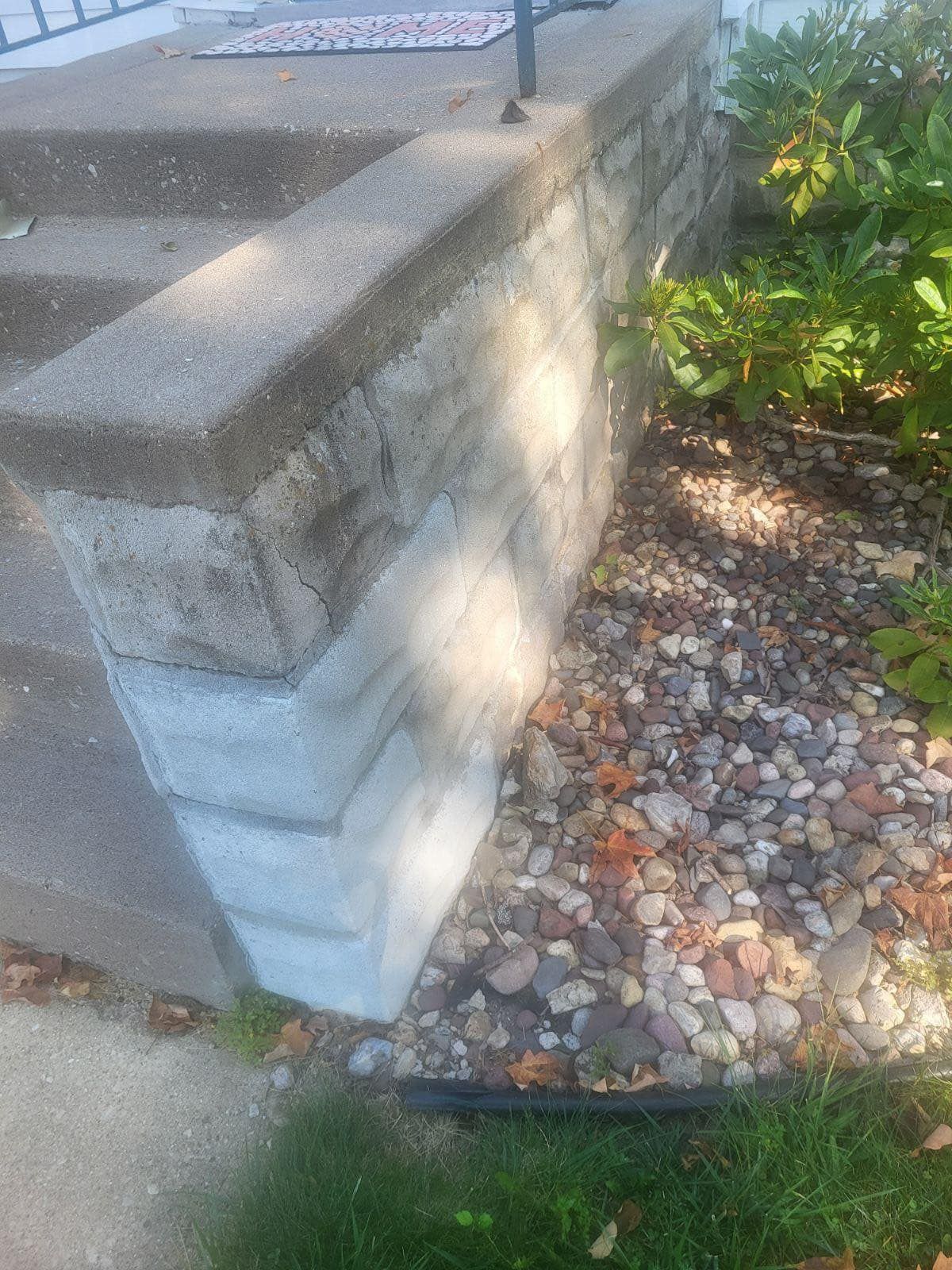 Concrete steps with a low retaining wall next to a rock bed and greenery.