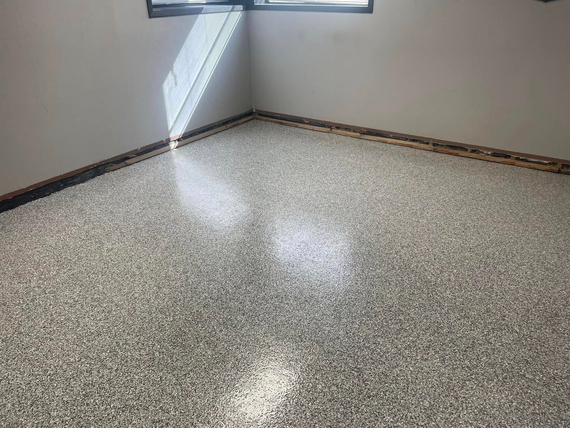 Epoxy-coated floor with speckled gray and white chips. Light streams in from a window, highlighting the texture.