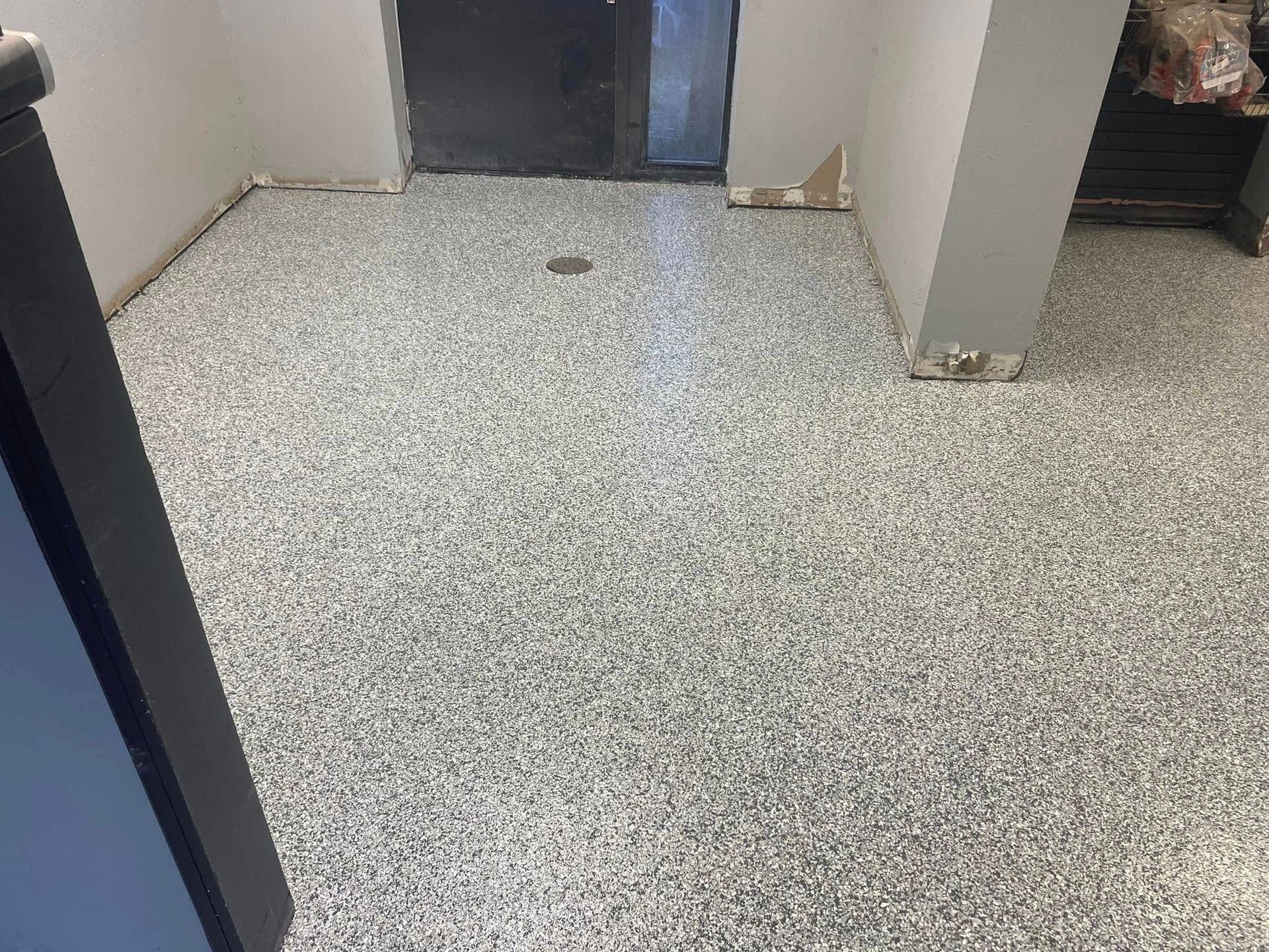 Room with a speckled gray epoxy floor, white walls, and a black door.